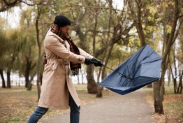 Man with blue umbrella caught in gust of wind outdoors