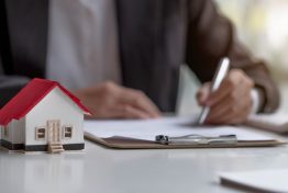 Real estate agents work at desks in rooms with paperwork and house designs to introduce clients.